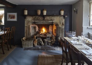 A cozy room with a fireplace, wooden chairs, a dining table set with glasses and cutlery, and a framed picture on the wall.