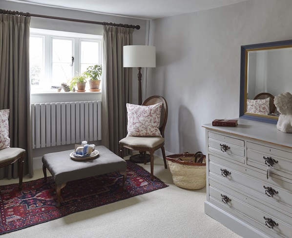A room with a window, a chair, a table with a tray, a lamp, a dresser, and a mirror.