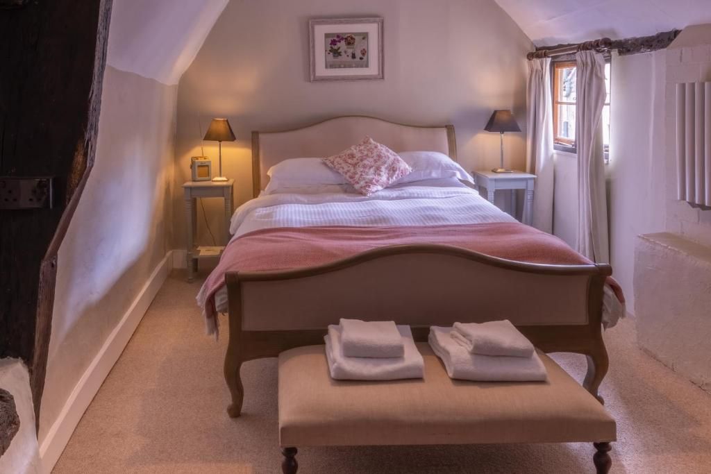 Un dormitorio con una cama individual, mesitas de noche, un banco con toallas y un cuadro en la pared.