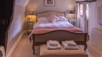 Un dormitorio con una cama individual, mesitas de noche, un banco con toallas y un cuadro en la pared.