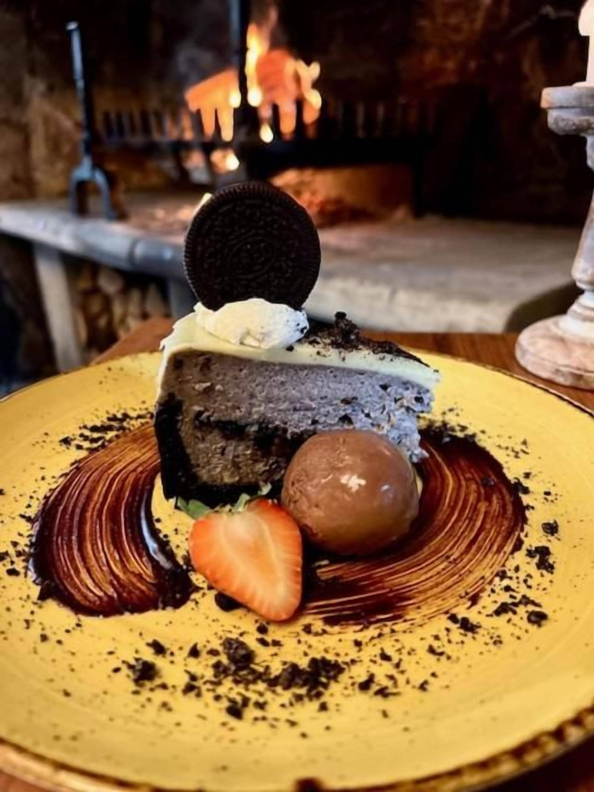 A dessert on a yellow plate with a chocolate cake, an Oreo cookie, a scoop of ice cream, and a strawberry.