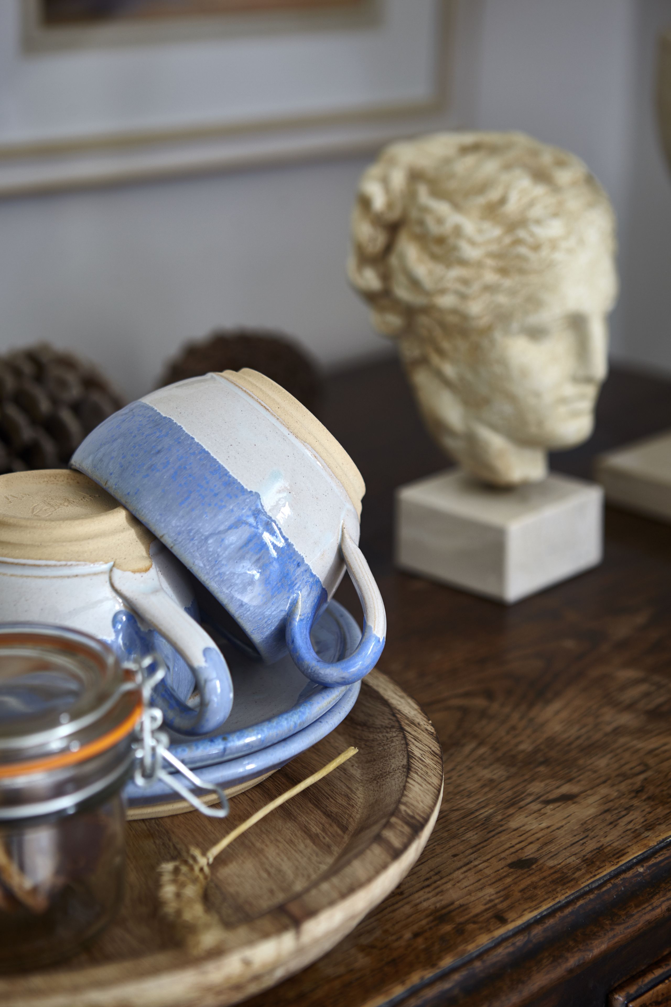 Une tasse en céramique avec un anse bleue et un bocal en verre, le tout posé sur un plateau en bois.