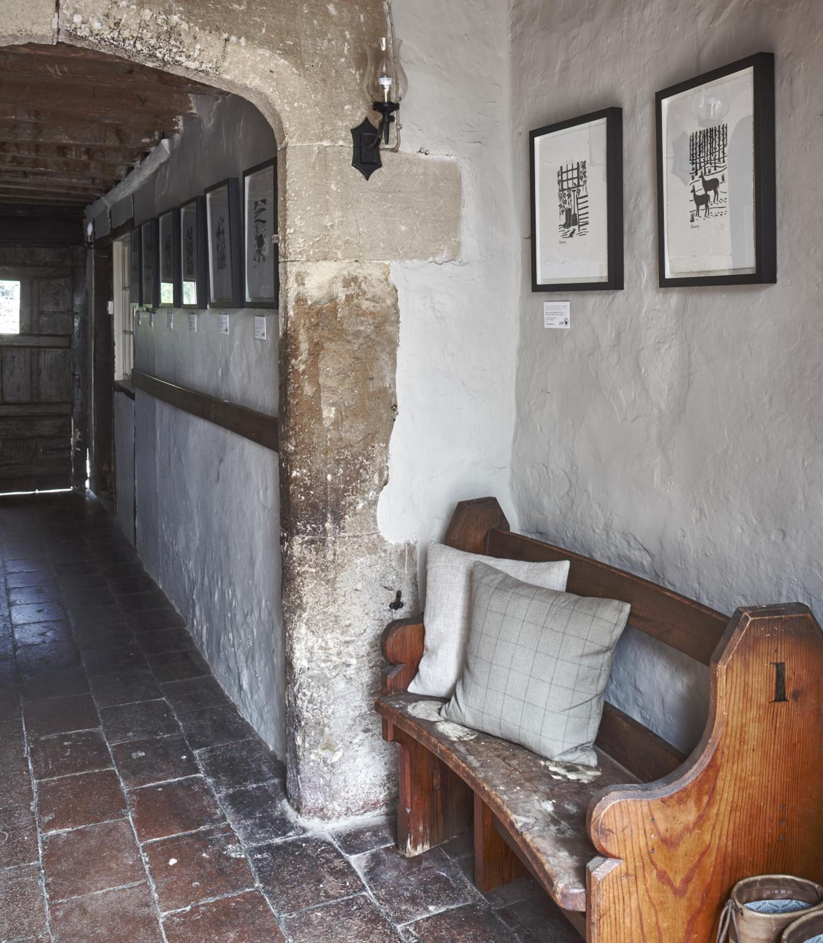 A corridor with a bench, framed pictures on the wall, and a stone floor.