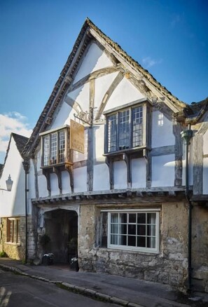 A traditional half-timbered house with a steeply pitched roof, a stone foundation, and a large window with multiple panes. - Sign of the Angel (Chippenham)