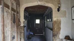 A narrow hallway with a rustic wooden door on the left, a bench on the right, and a view into a room at the end. - Sign of the Angel (Chippenham)