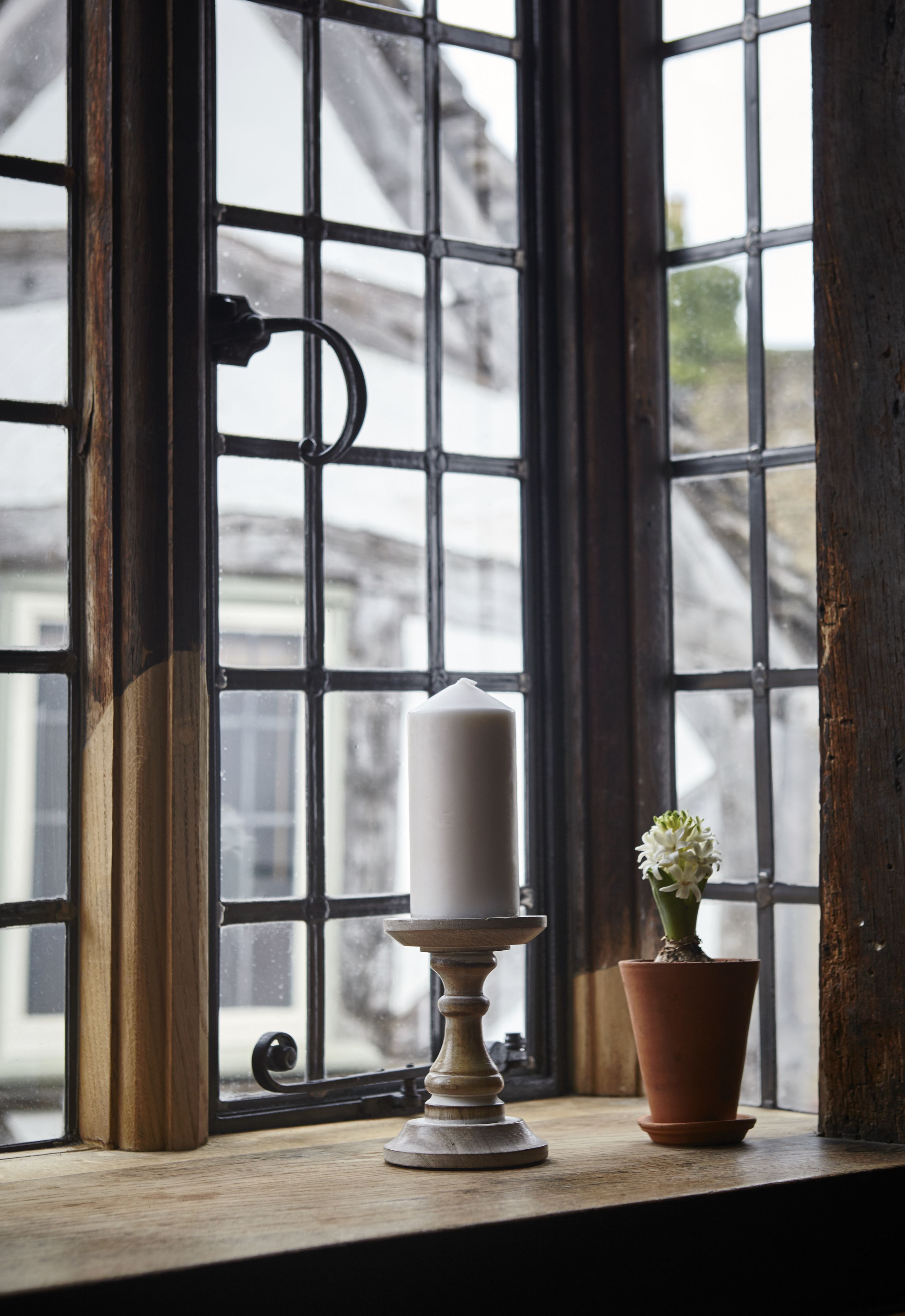 A candle on a window sill with a potted plant beside it.