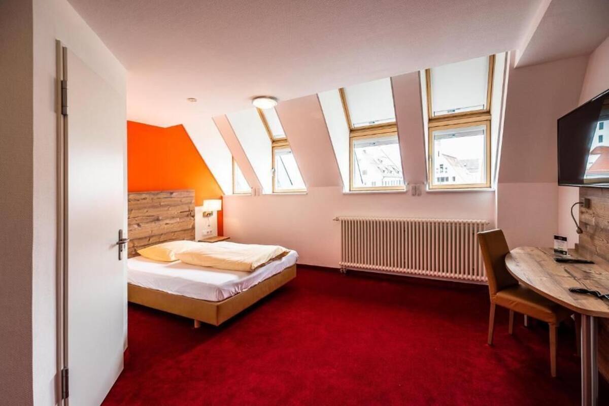 A bedroom with a bed, a desk, and a chair. There are skylights and a radiator.
