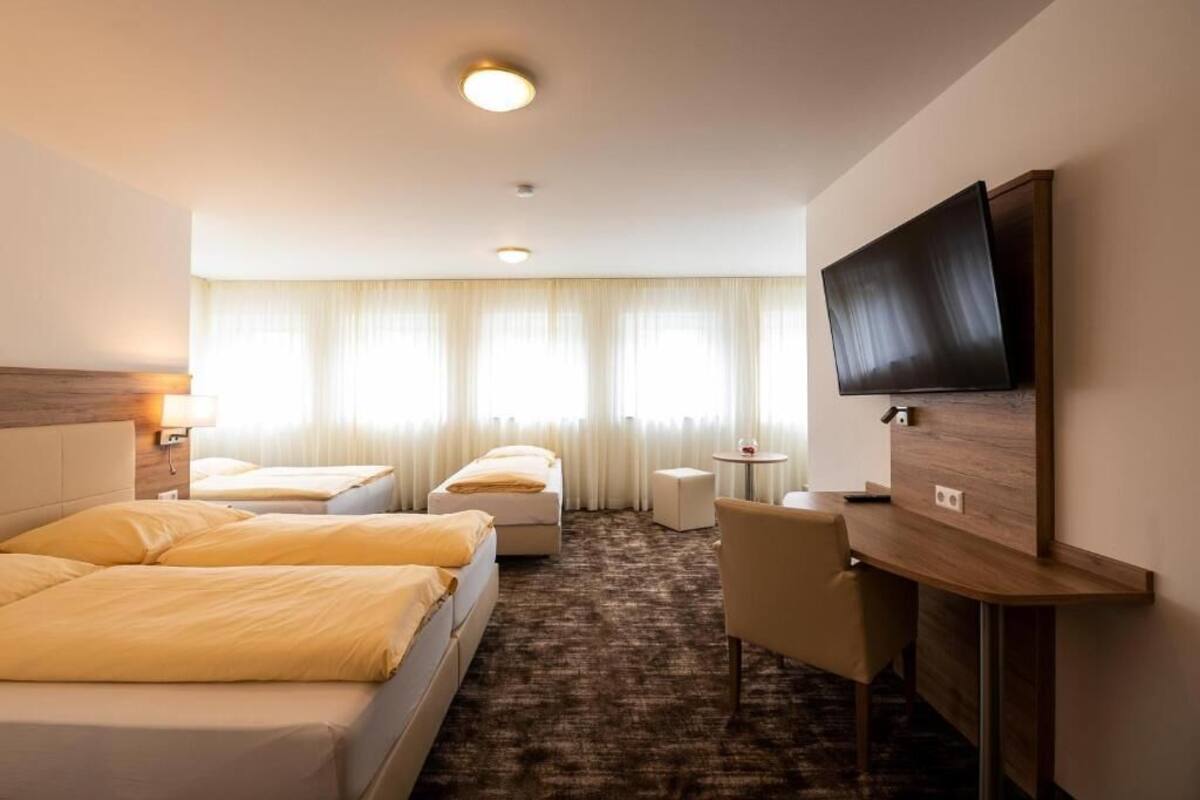 A hotel room with two beds, a desk, a chair, a TV, and a window with curtains.