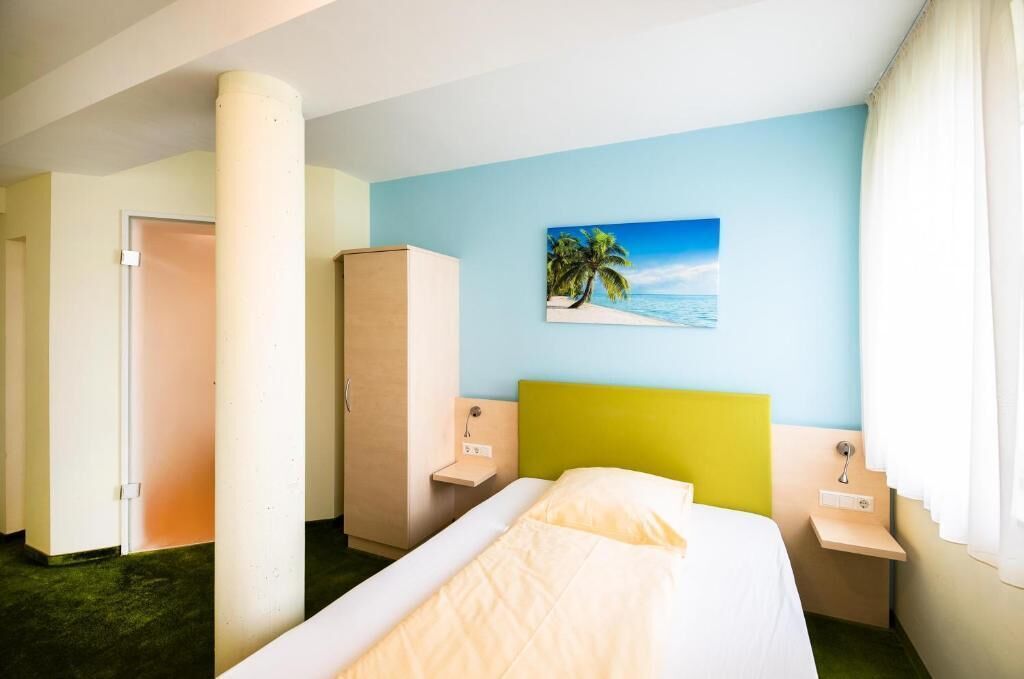 A hotel room with a bed, a nightstand, a wardrobe, and a painting of a beach scene on the wall.