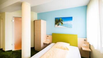 A hotel room with a bed, a nightstand, a wardrobe, and a painting of a beach scene on the wall.