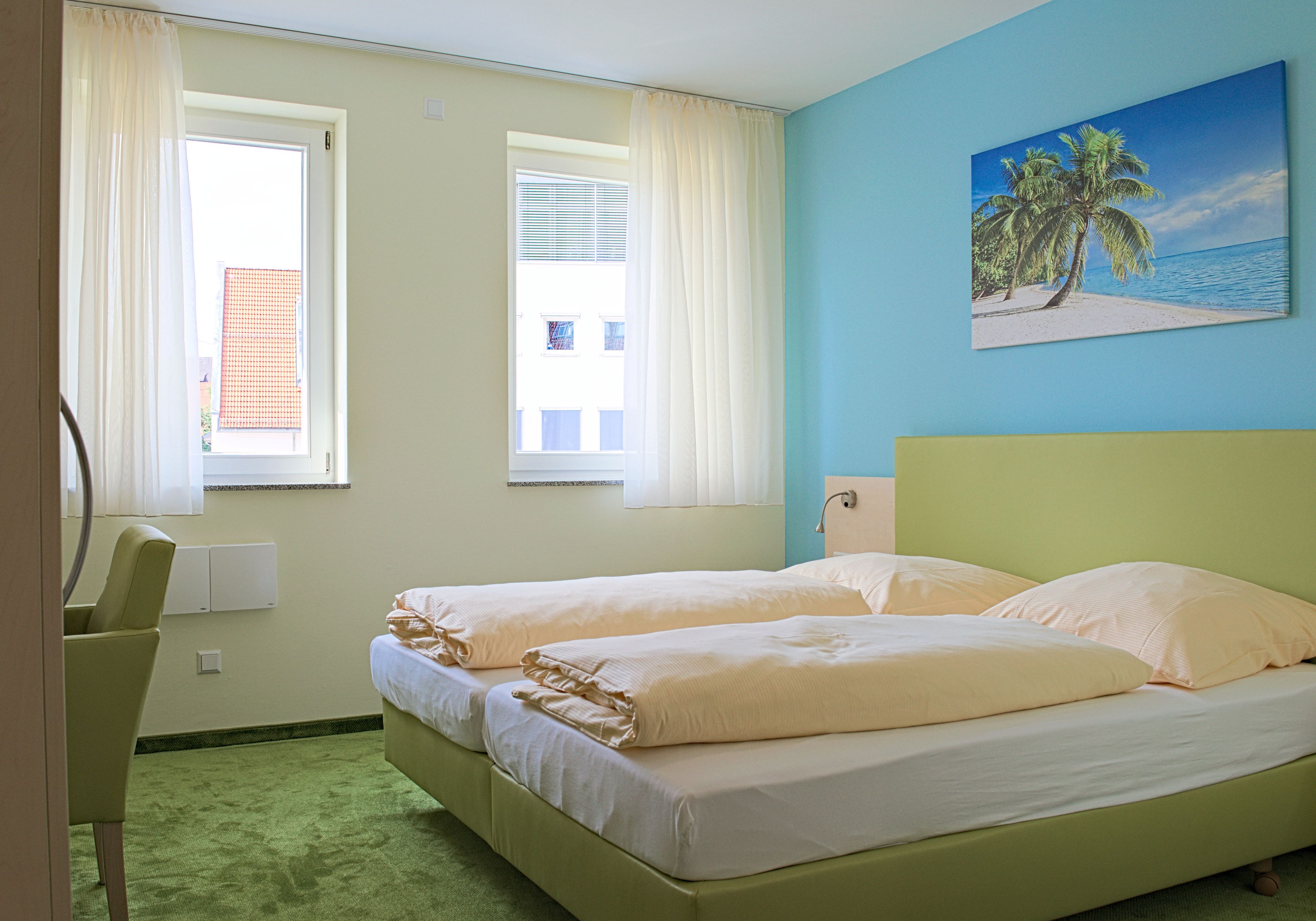 A room with two beds, a desk, and a painting of a beach scene.