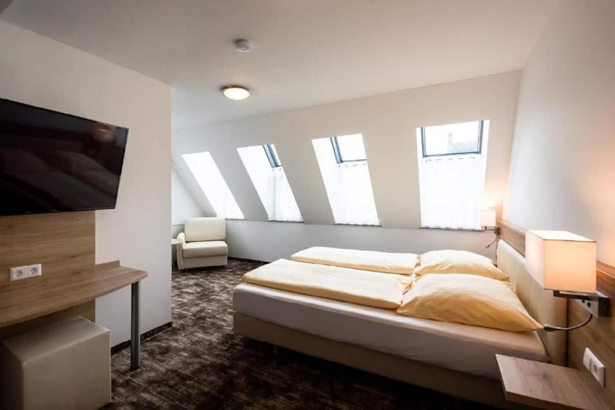 A hotel room with a bed, a TV, a desk, and skylights.
