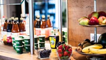 Una variedad de frutas y bebidas, como manzanas, plátanos, fresas, arándanos y botellas de jugo.