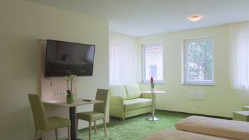 Camera d'albergo con tappeto verde, un letto, un divano, una TV e un piccolo tavolo con una pianta.