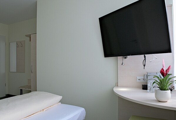 A hotel room with a bed, a mounted TV, a sink, and a potted plant.
