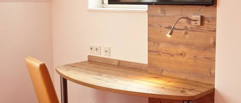 A small, modern room with a wooden desk, a chair, and a mounted TV.