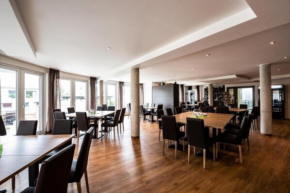 Un vaste espace dédié à la salle à manger, avec de nombreuses tables et chaises, de grandes fenêtres et un aménagement intérieur moderne.