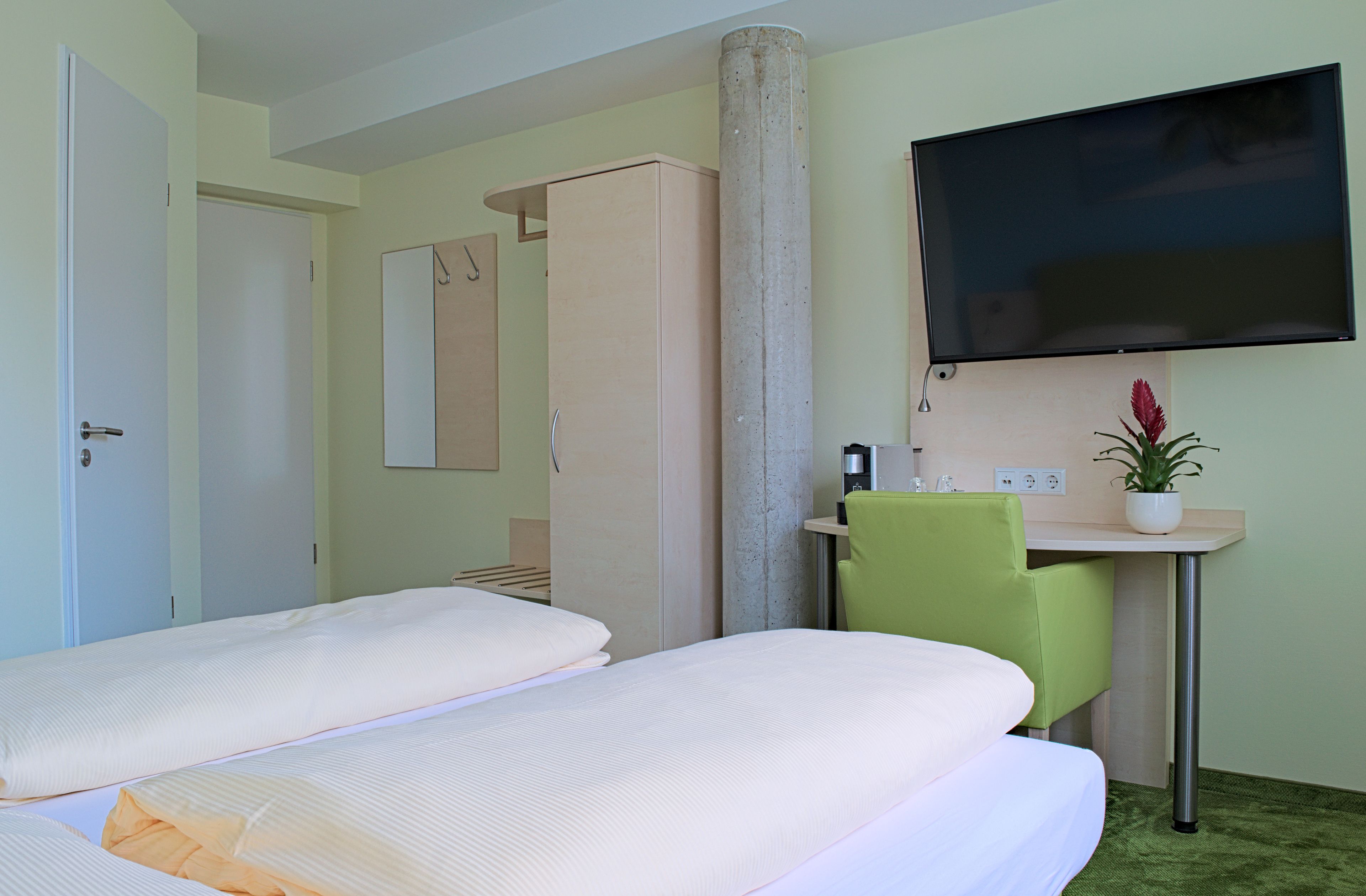 Une chambre d’hôtel avec deux lits, un bureau, une chaise, une télévision et une plante.