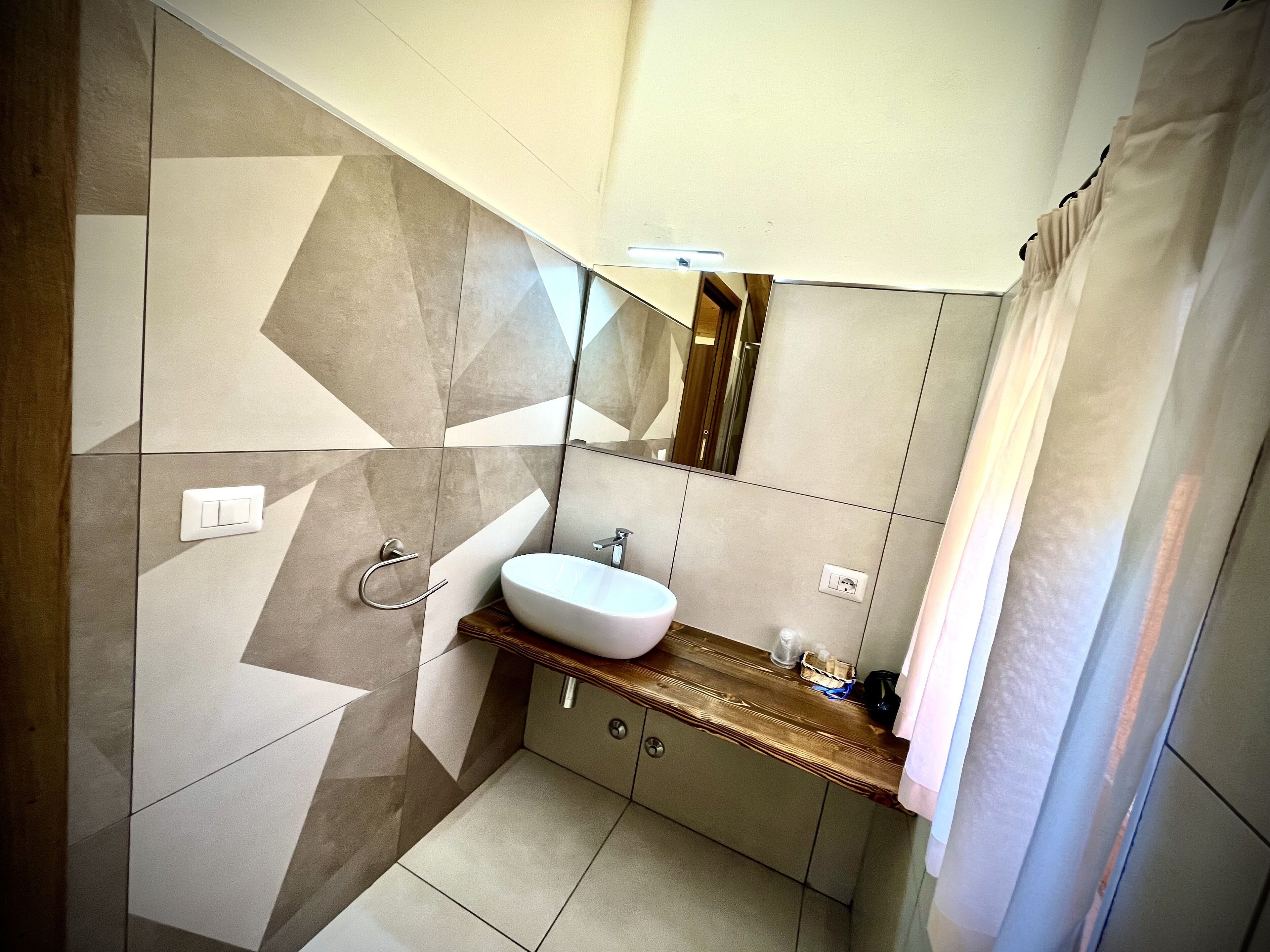 A modern bathroom with a white sink, wooden countertop, and geometric patterned tiles.