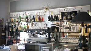 Una zona de bar con estantes llenos de botellas de licores, una máquina de café y una taza de café sobre la barra.