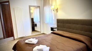 Una habitación de hotel con una cama grande, una mesita de noche, un espejo y una lámpara de pared.