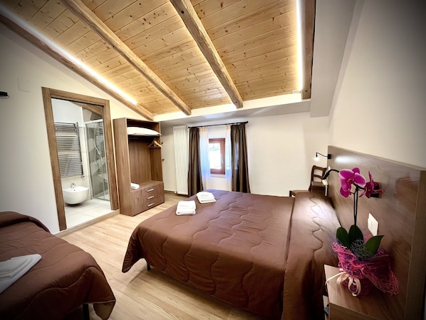 A bedroom with two beds, a wooden ceiling, a walk-in closet, a bathroom with a glass shower, and a window with curtains. - Hotel Pinguino (Pescasseroli)