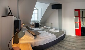 Een moderne slaapkamer met een groot bed, een bureau en een aan de muur bevestigde televisie.
