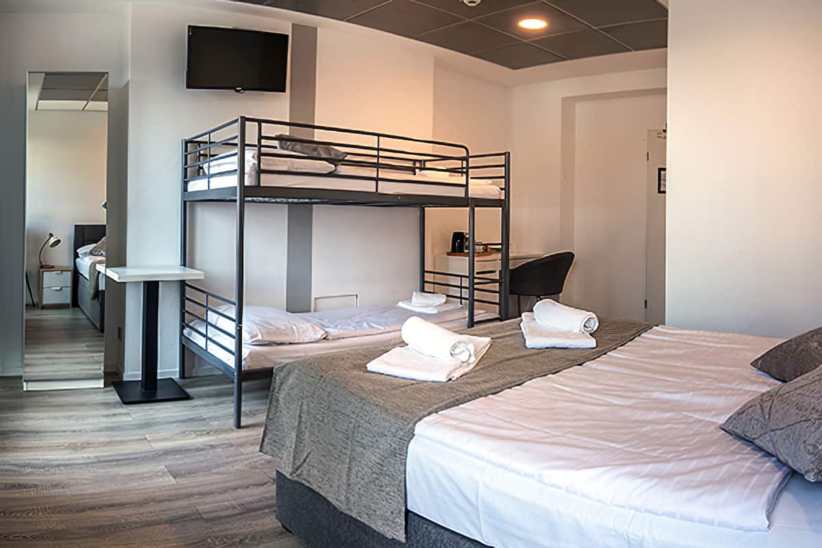 Habitación de hotel con literas, un escritorio, una silla y un televisor en la pared.