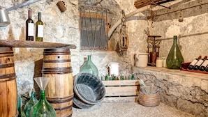 A rustic cellar with wooden barrels, green glass bottles, and a metal rack holding wine bottles. - Casa Nannina (Meta)