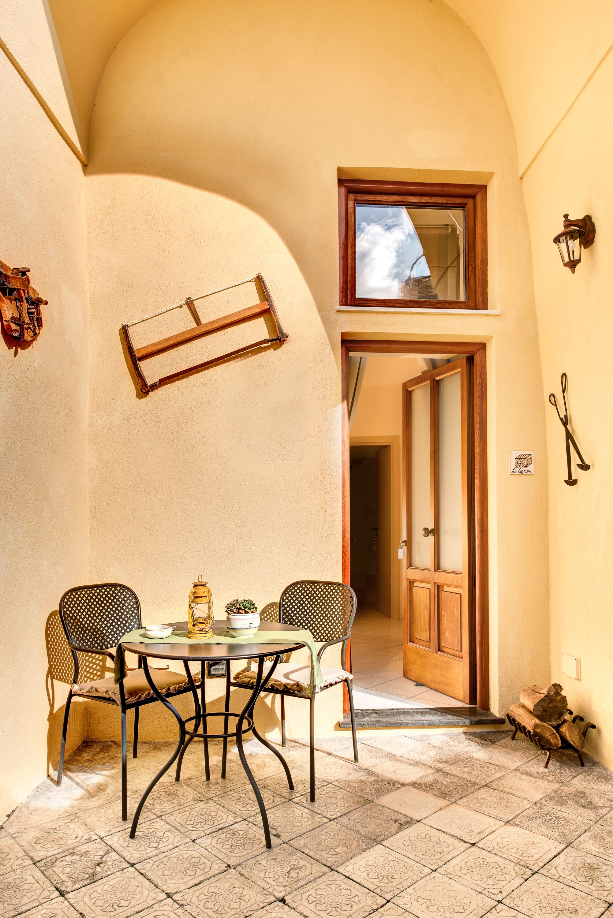 Un espacio al aire libre acogedor con una mesa redonda y dos sillas, una puerta de madera y una ventana pequeña.