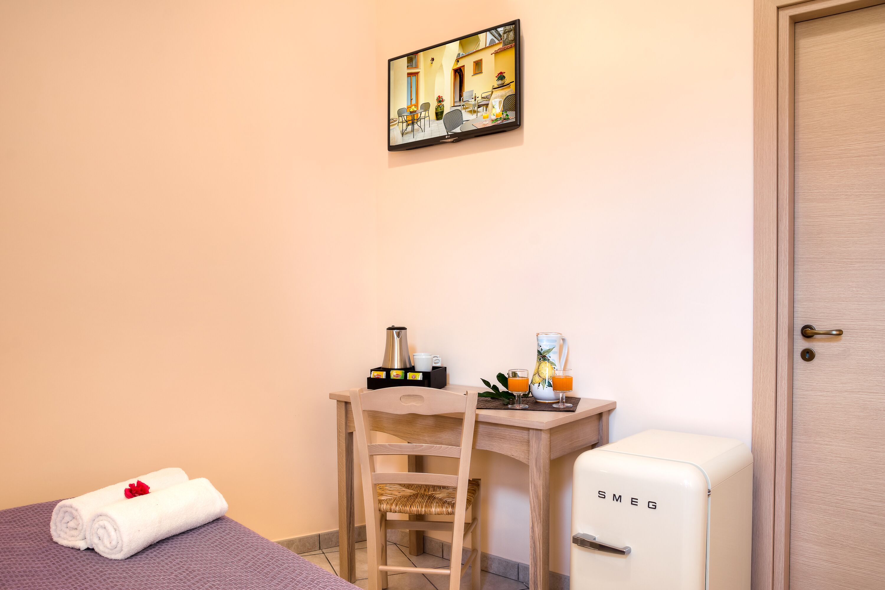 A small room with a bed, a wooden desk, a chair, a small refrigerator, and a painting on the wall.