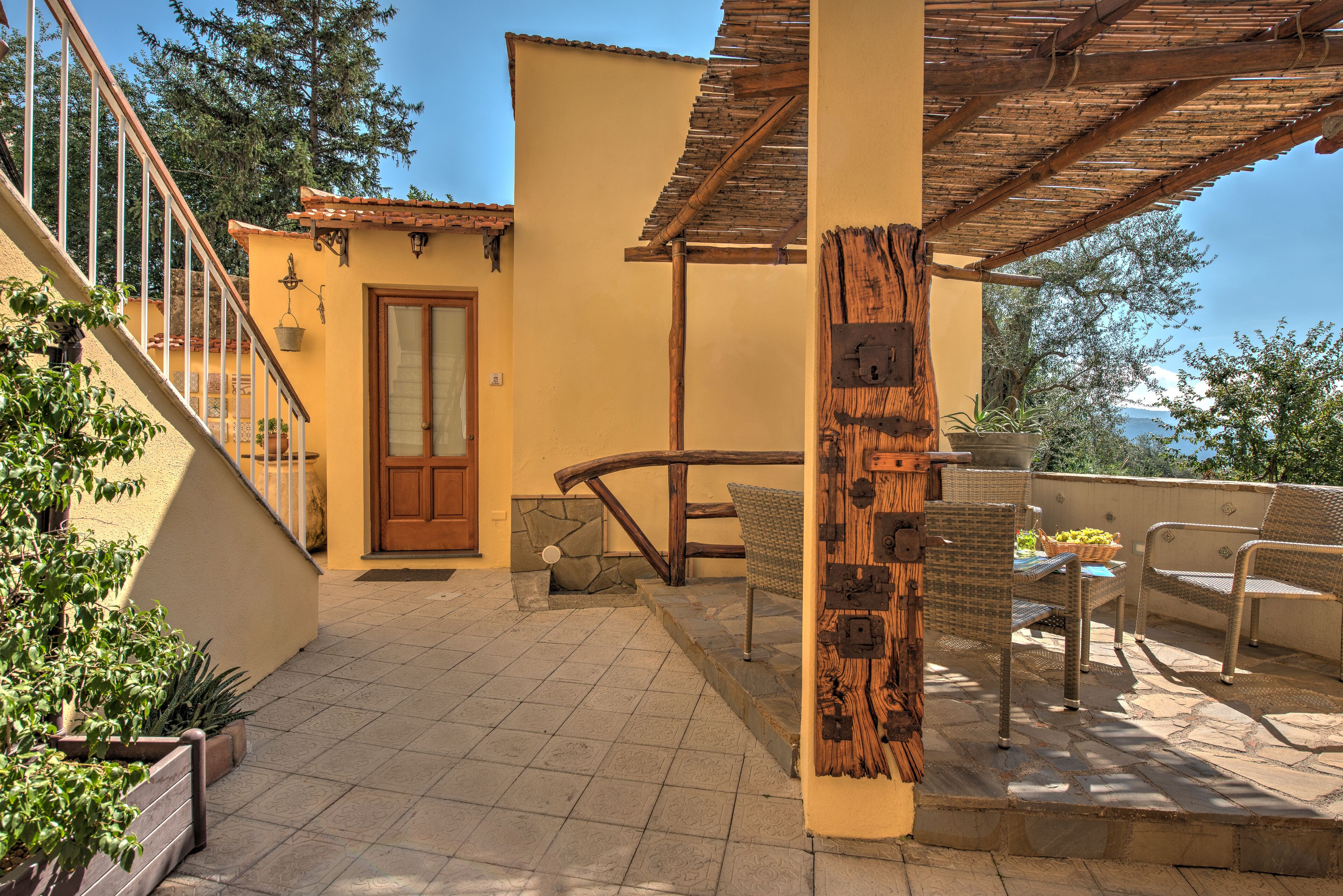 Eine sonnendurchflutete Terrasse mit Holz-Pergola, einer Steintreppe und Gartenmöbeln.