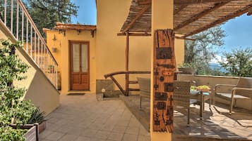 Eine sonnendurchflutete Terrasse mit Holz-Pergola, einer Steintreppe und Gartenmöbeln.