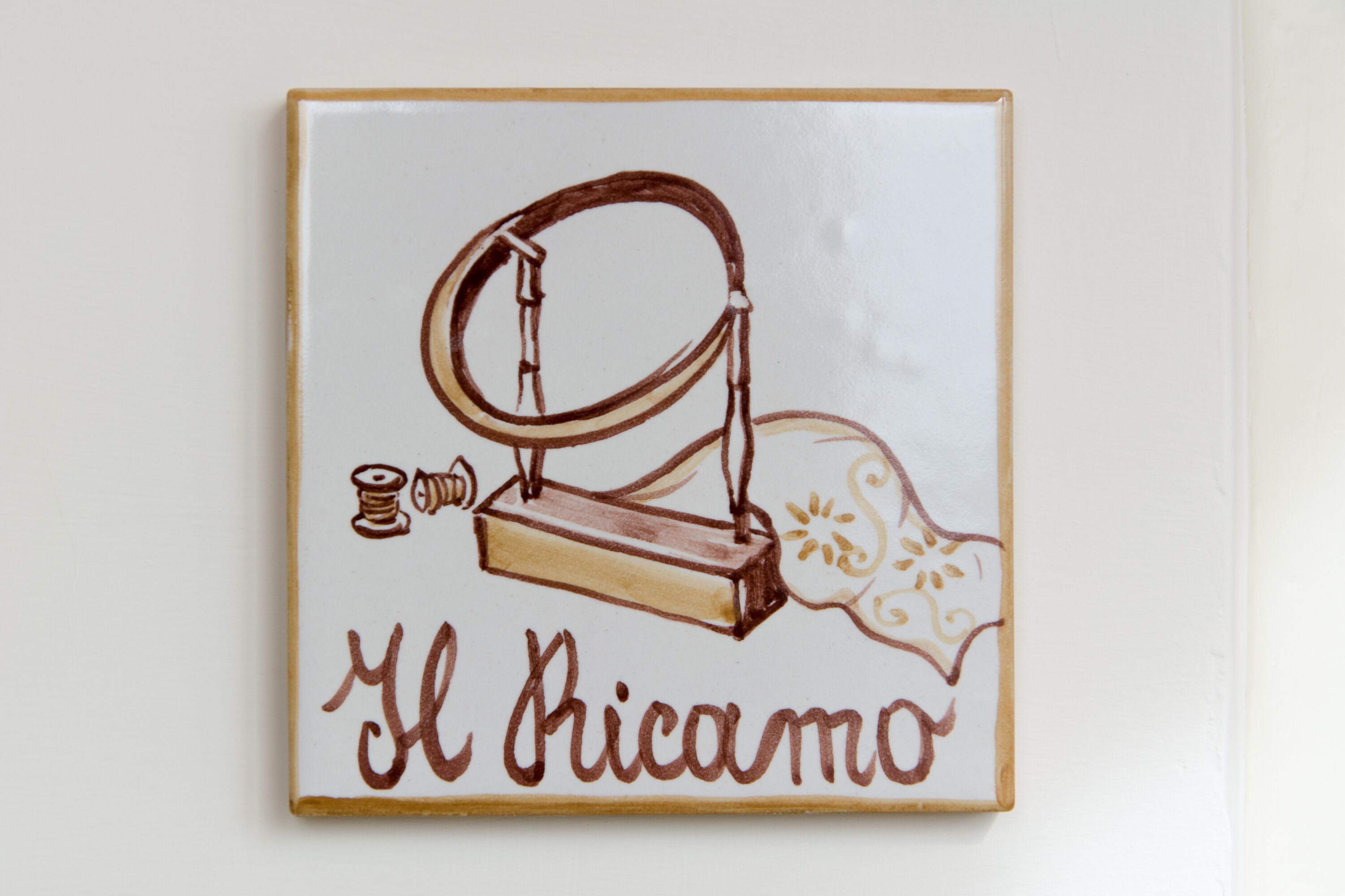 A ceramic tile with a sewing machine illustration and the text "El Ricamo".