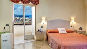 A hotel room with a bed, a nightstand, a lamp, a minibar, and a view of the city through a door. - Casa Nannina (Meta)