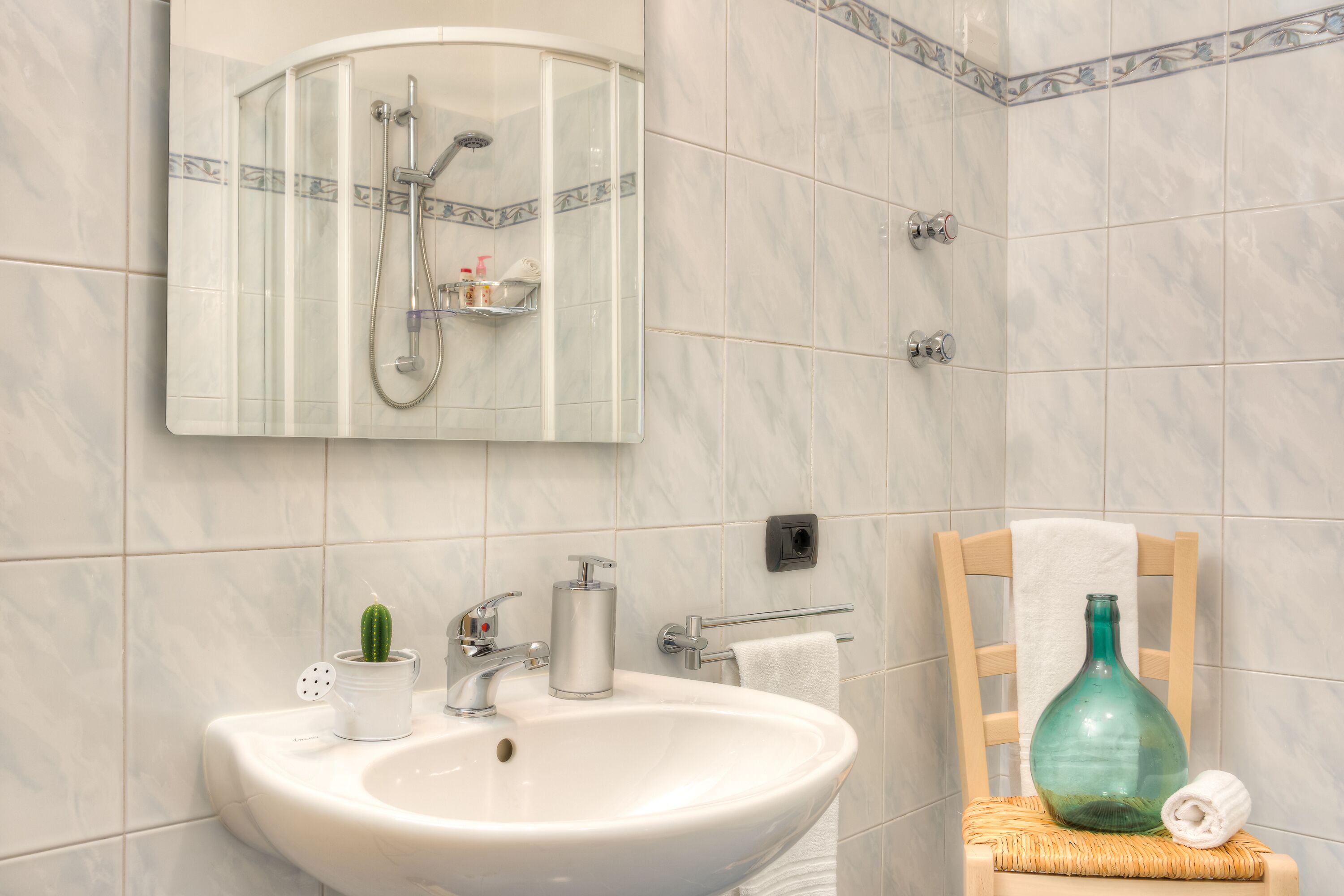 Ein Badezimmer mit weißem Waschbecken, einem Spiegel, einer Dusche und einem Handtuchhalter.