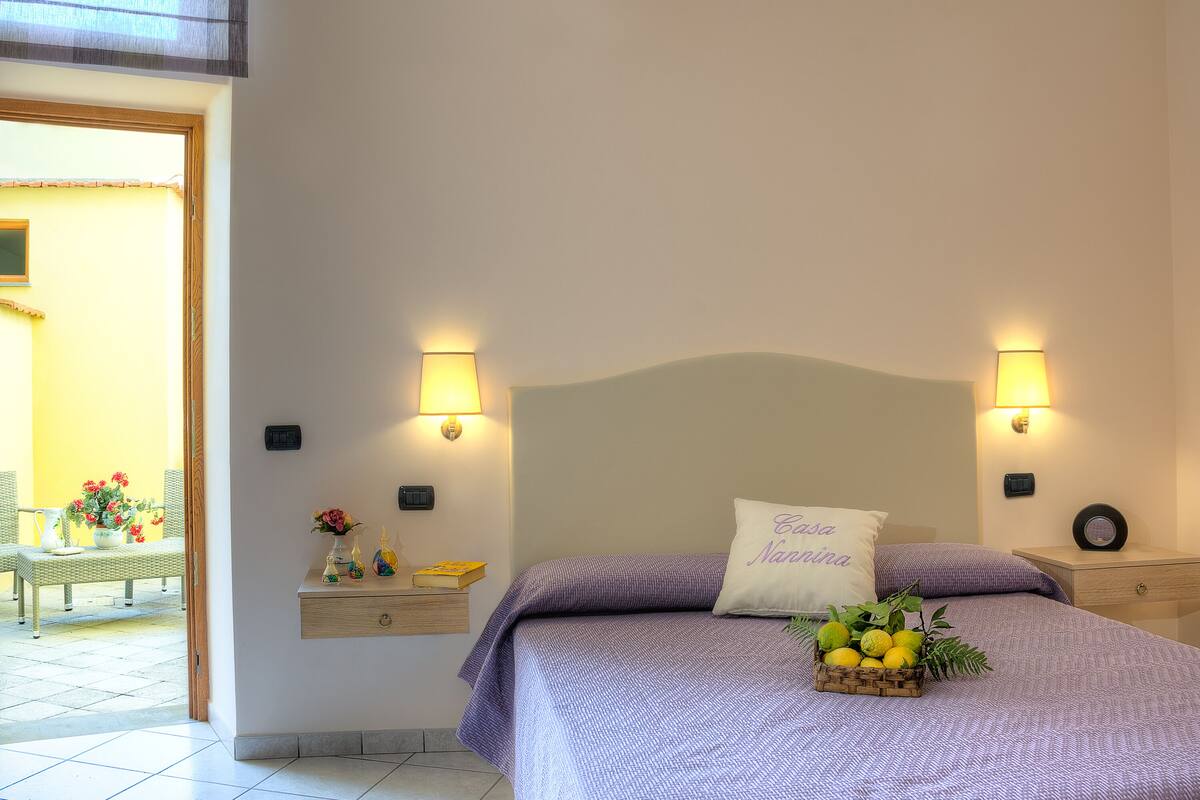 A bedroom with a bed, two bedside tables, a nightstand, a wall-mounted lamp, and a small table with a vase of flowers.