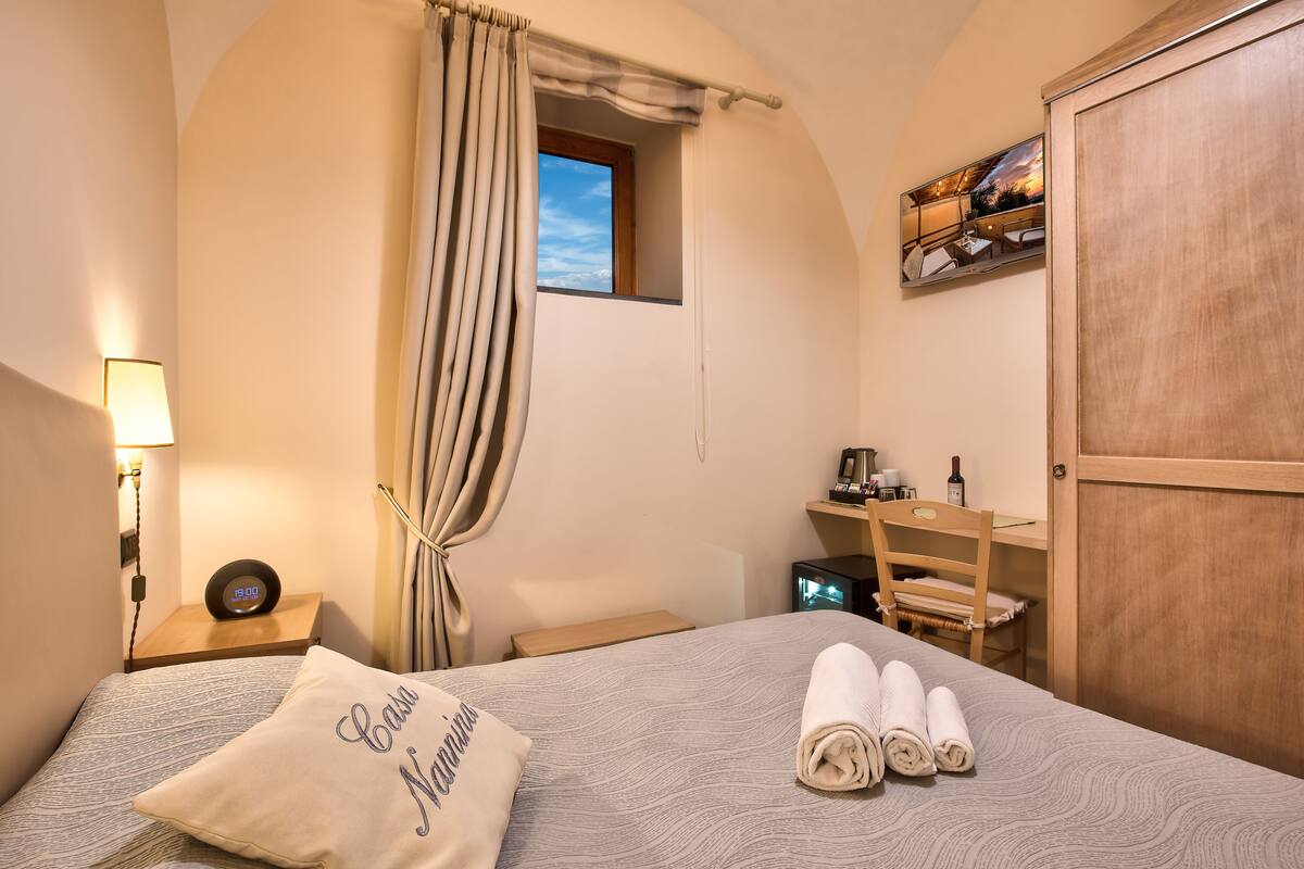A bedroom with a bed, a nightstand, a desk, a chair, a wardrobe, and a window with curtains.