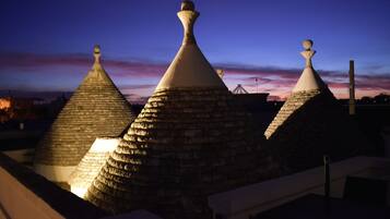A row of traditional conical-roofed buildings with stone walls and a flat roof, illuminated by artificial lighting.