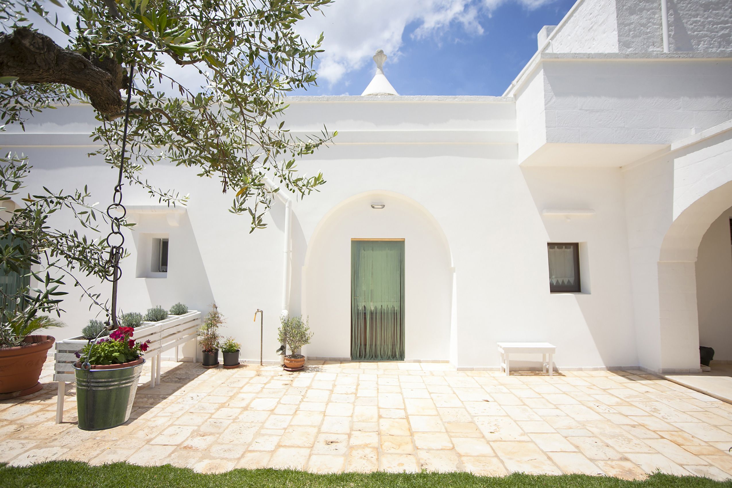 Un patio con un edificio blanco, una puerta verde y plantas en macetas.