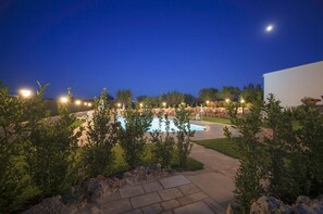 A nighttime view of a landscaped outdoor area with a swimming pool, surrounded by greenery and illuminated by ambient lighting. - Coppola di Seta (Locorotondo)