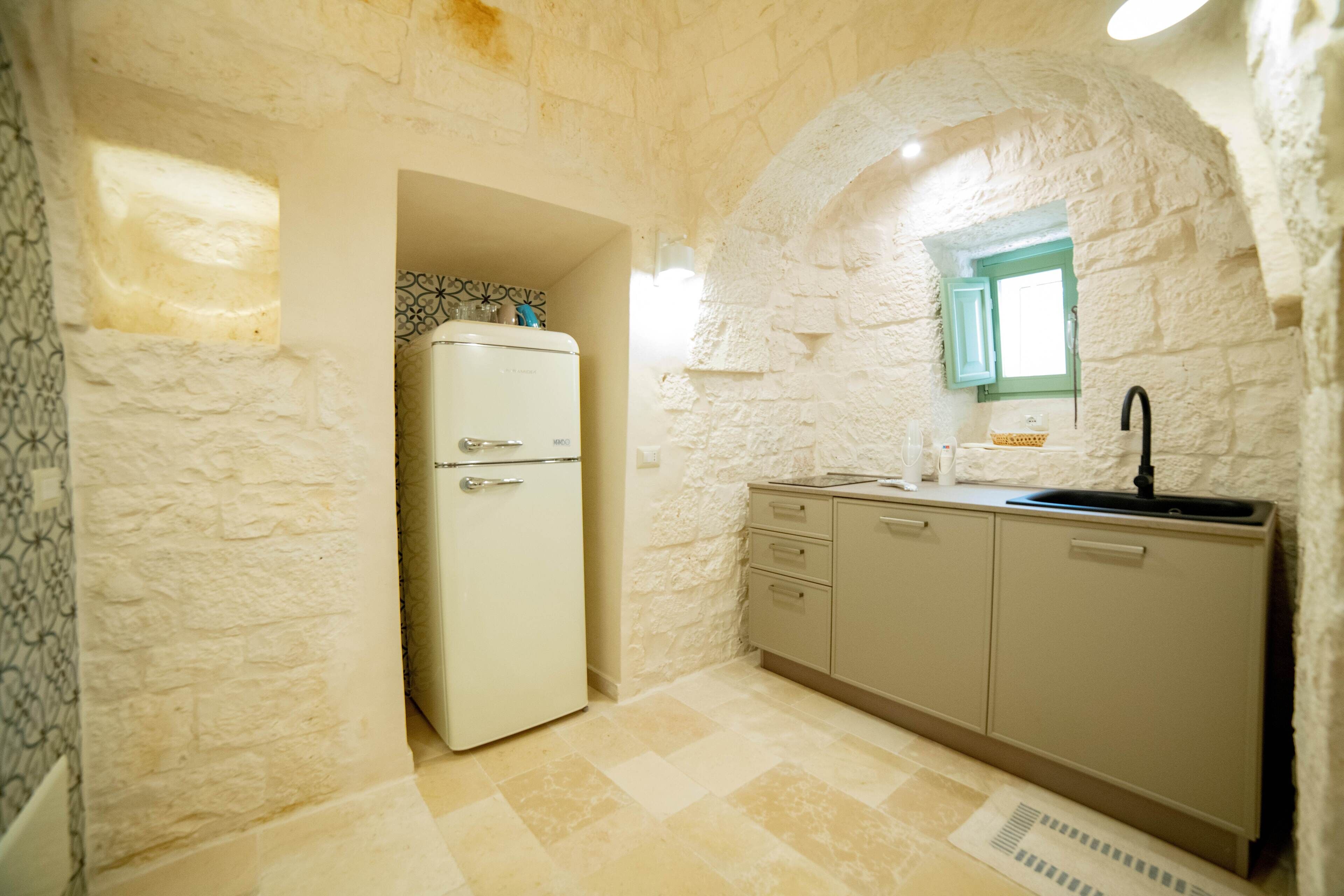 A compact kitchen with a white refrigerator, a sink, and a window with a blue frame.