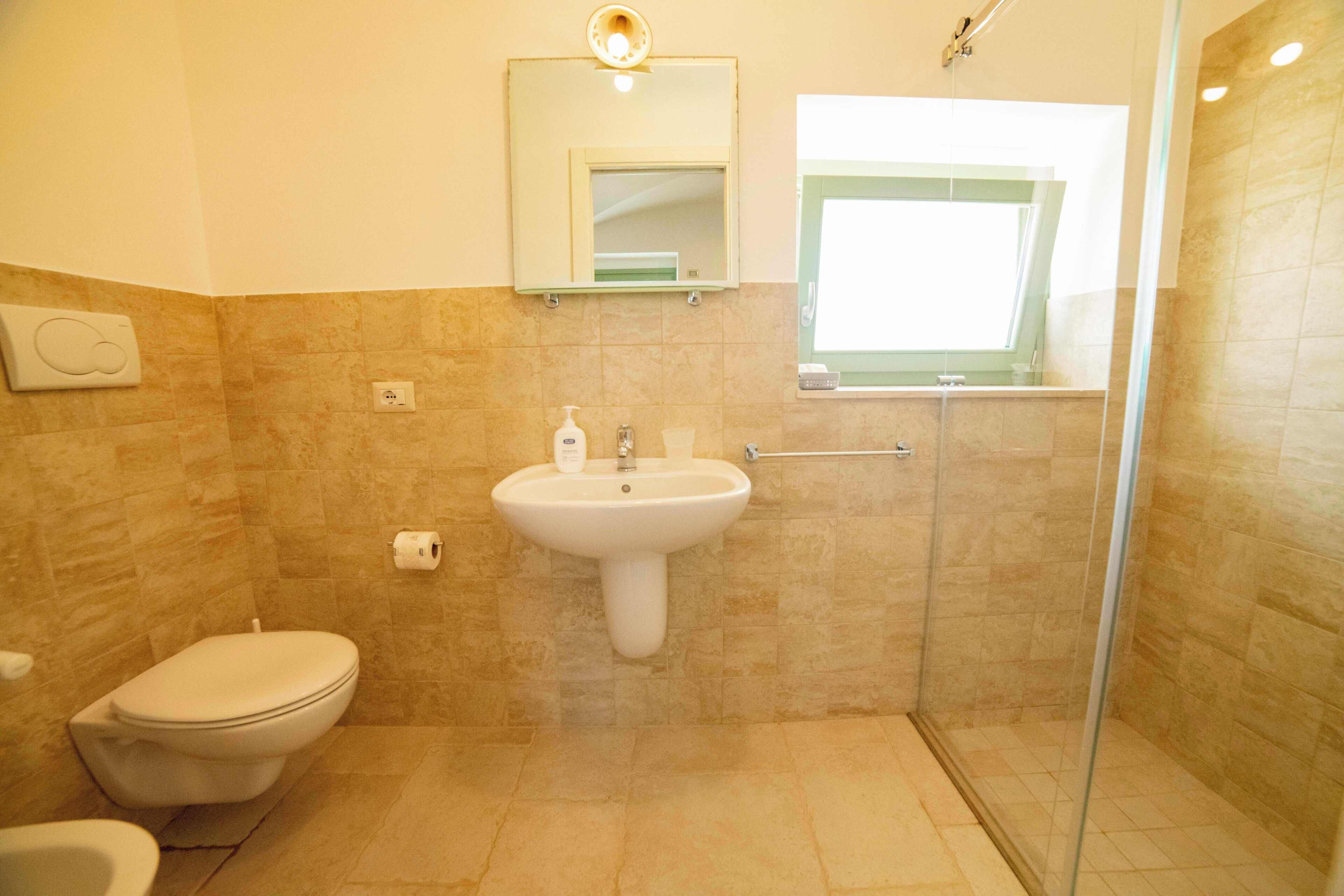 Un baño con inodoro, lavamanos y ducha con mampara de vidrio.