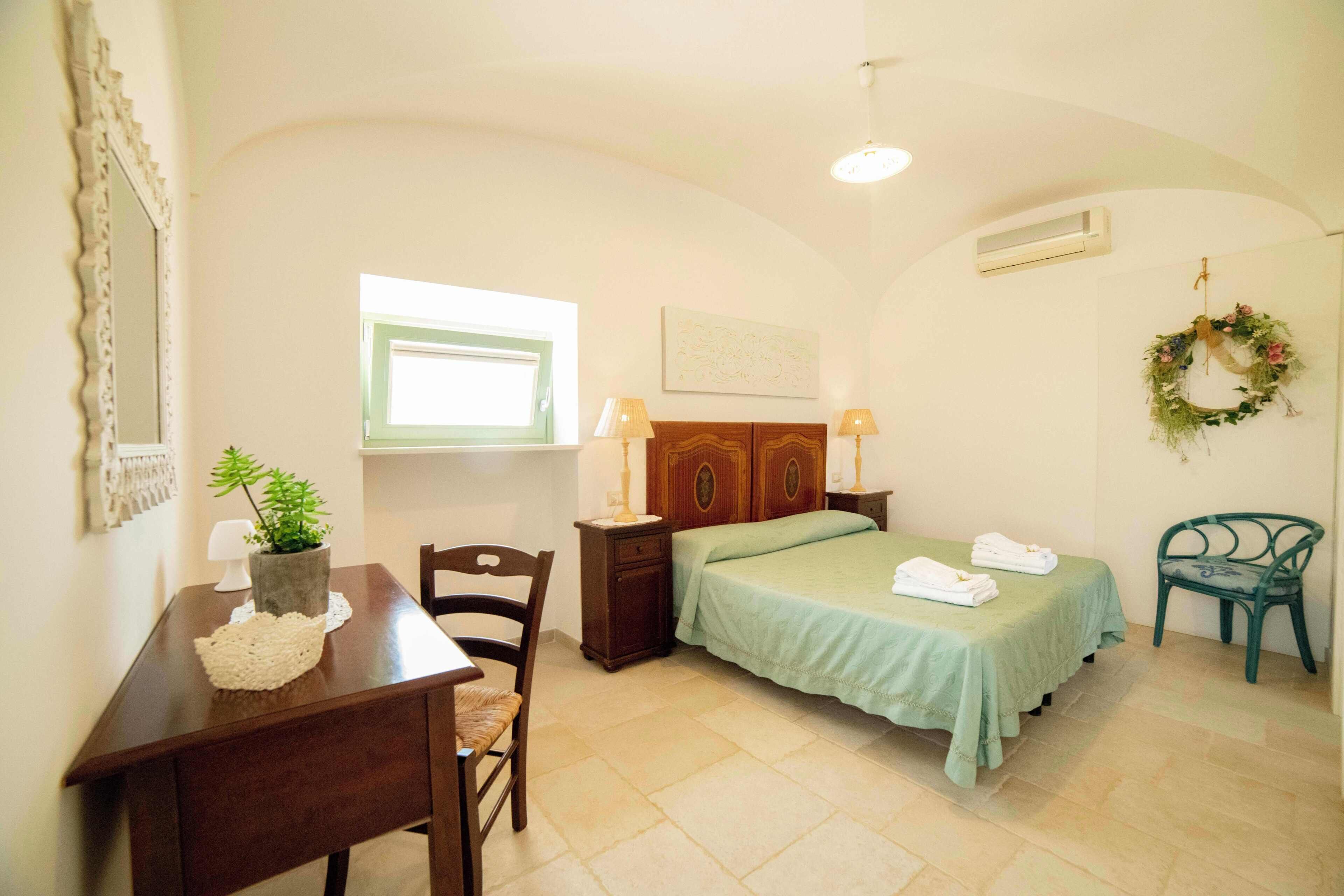 A bedroom with a bed, bedside tables, a desk, a chair, a window, and a wall-mounted air conditioner.