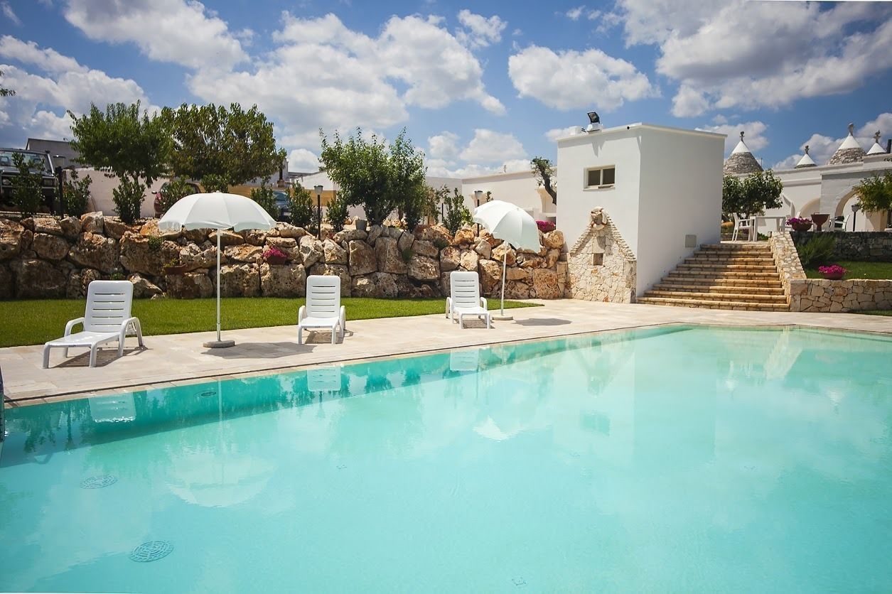 Ein Pool mit Liegestühlen und Sonnenschirmen, eine Steinmauer und ein Gebäude mit einer Kuppel.