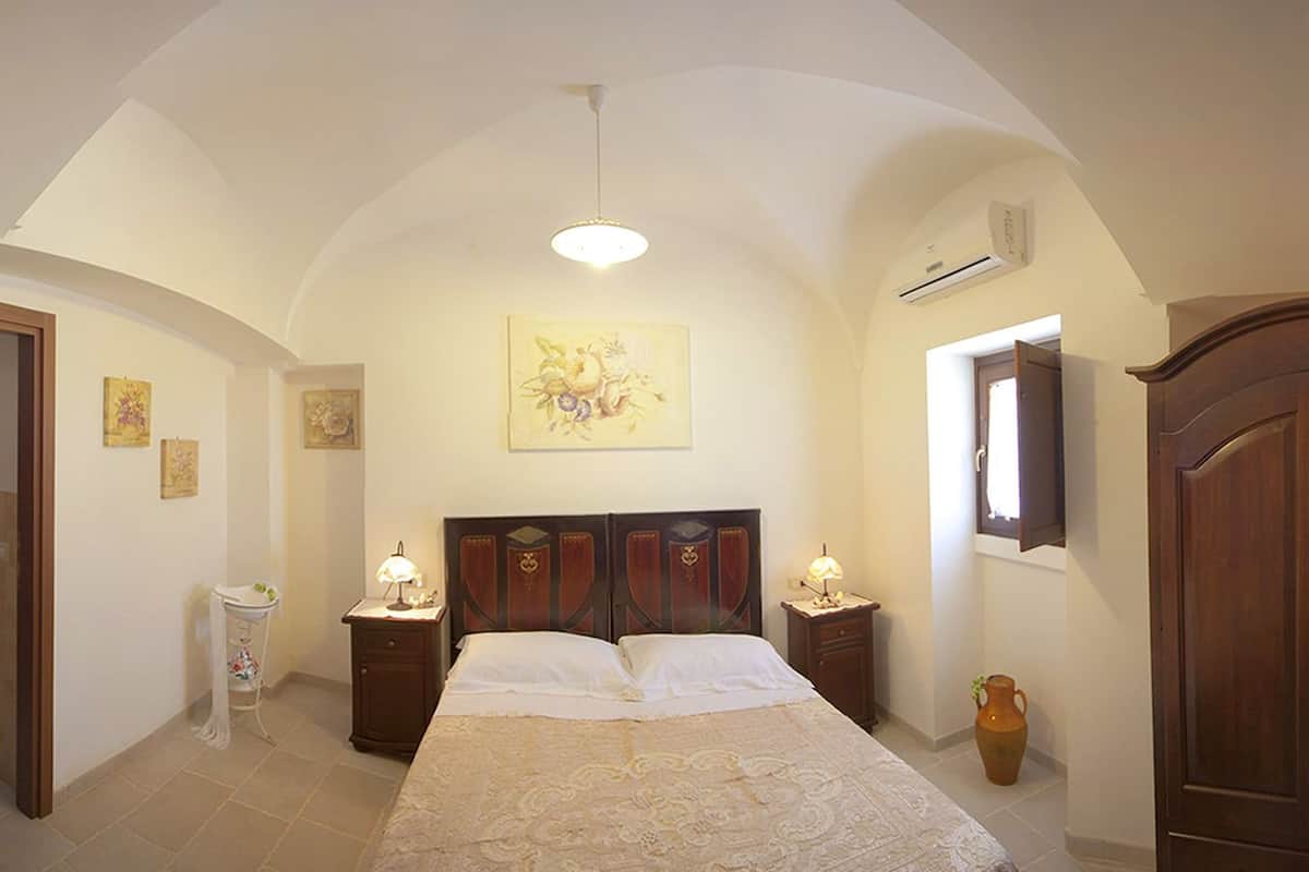 A bedroom with a large bed, two bedside tables, a wardrobe, a ceiling light, and a painting on the wall.