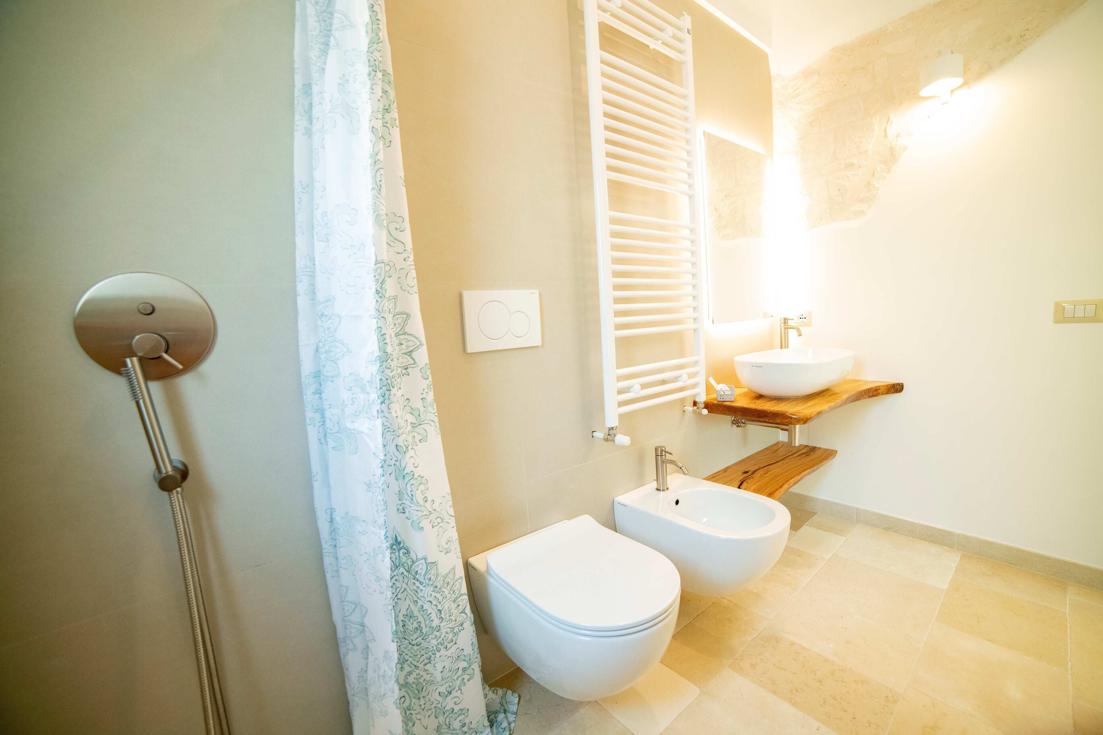 Un baño con ducha, dos inodoros, un lavabo y un estante de madera.