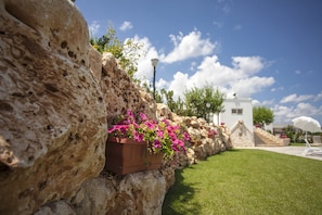 A stone wall with a flower planter, a white building with steps, and a clear blue sky. - Coppola di Seta (Locorotondo)