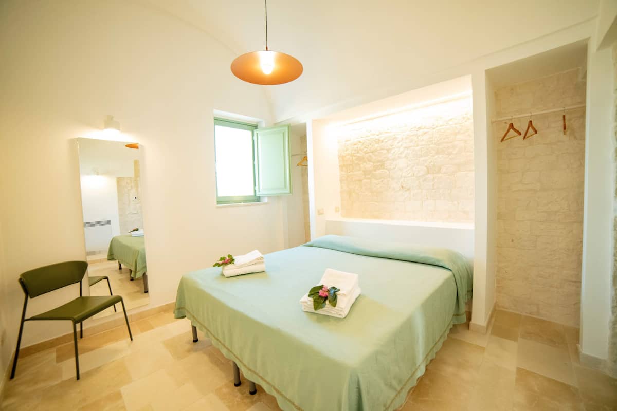 A bedroom with a bed, a chair, a window, and a wall with a hanging rack.
