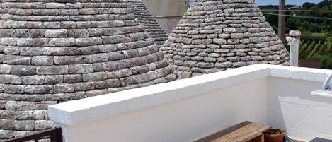 A rooftop terrace with stone conical structures, a wooden bench, and a metal table.